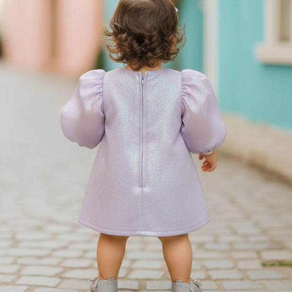 Child wearing a light purple dress with puffed sleeves on a cobblestone street.
