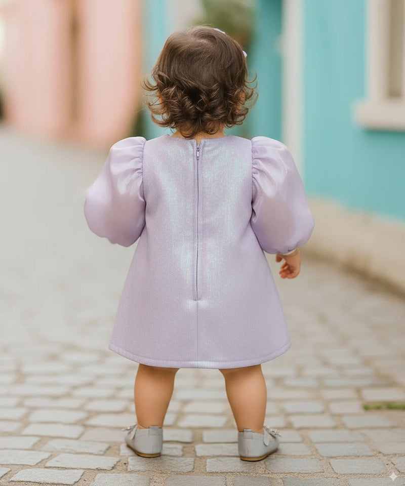 Child wearing a light purple dress with puffed sleeves on a cobblestone street.