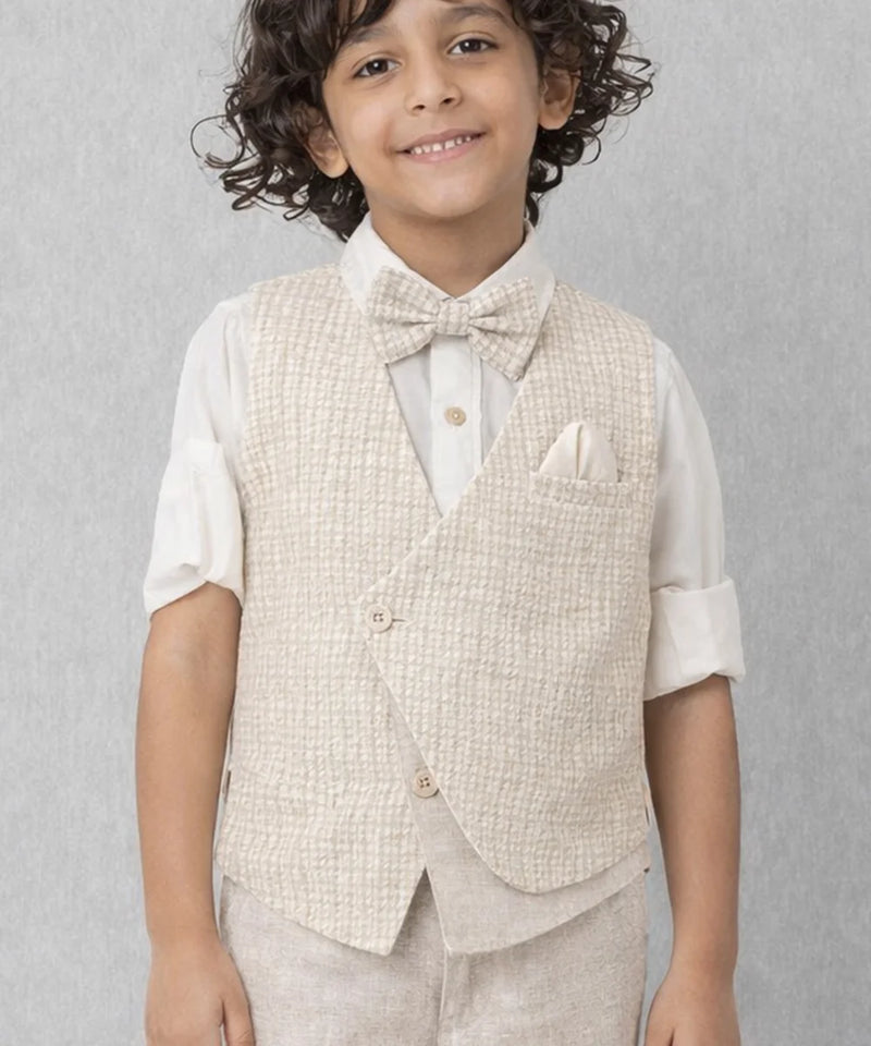 Young boy wearing a beige vest and bow tie against a gray background