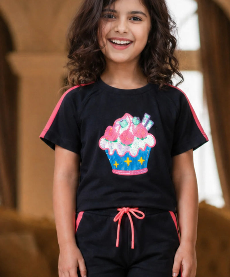 Child wearing a black t-shirt with a colorful cupcake design and black pants with pink accents.