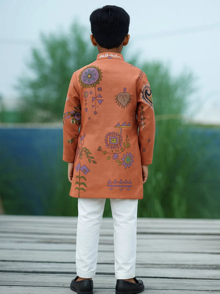 Child wearing an orange embroidered kurta with white pants on a wooden deck.