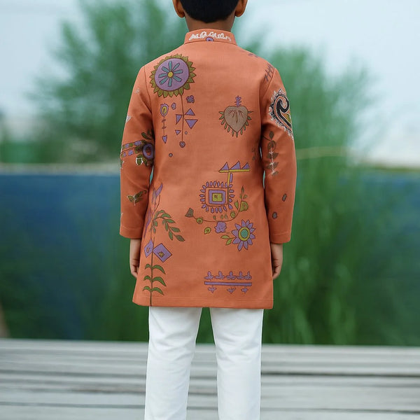 Child wearing an orange embroidered kurta with white pants on a wooden deck.