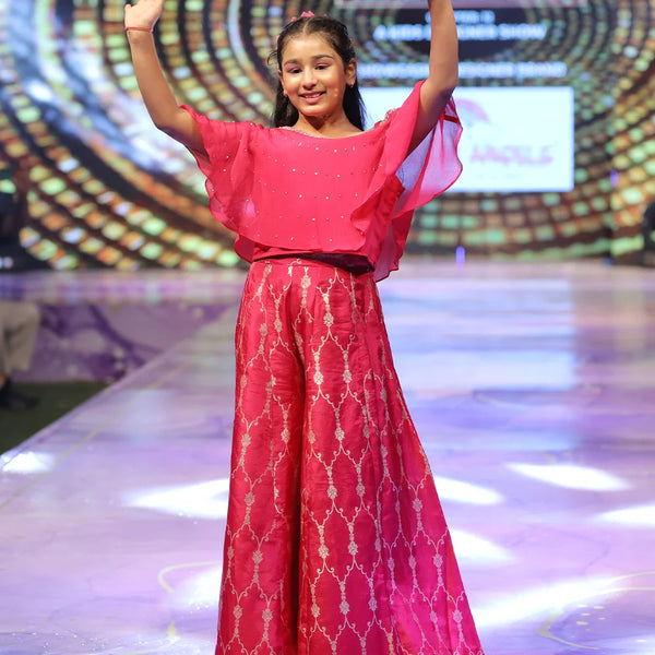 Young girl in a red sharara outfit with a patterned design on a stage with a colorful background