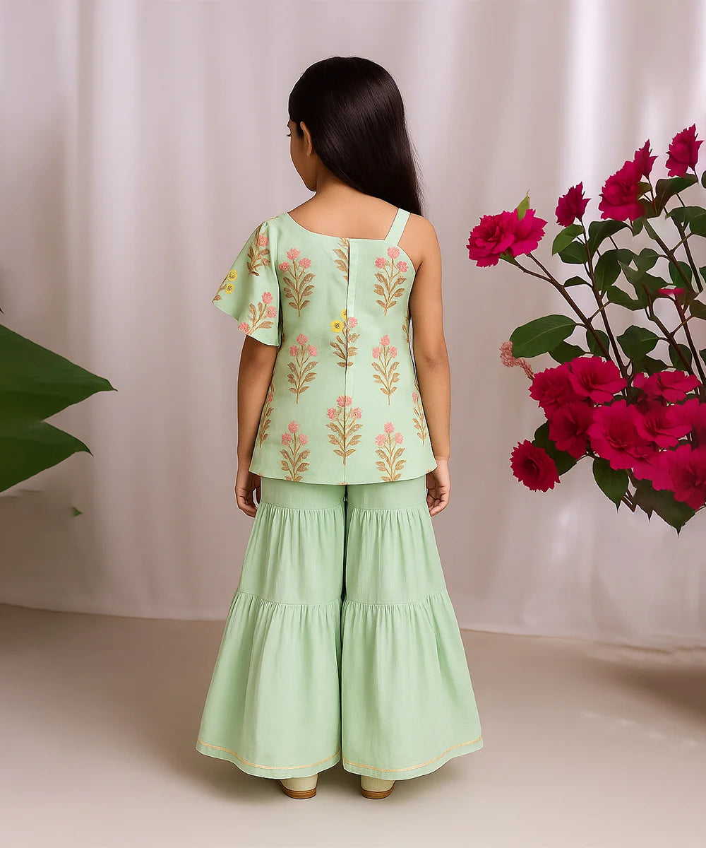 Woman wearing a light green outfit with floral patterns, standing against a white curtain with pink flowers.