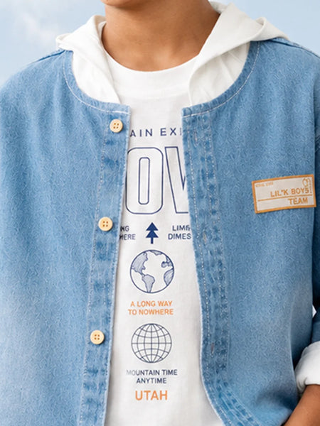 A close-up of a person wearing a light blue denim jacket over a white graphic t-shirt with a white hood, featuring a tan 'L.H.
