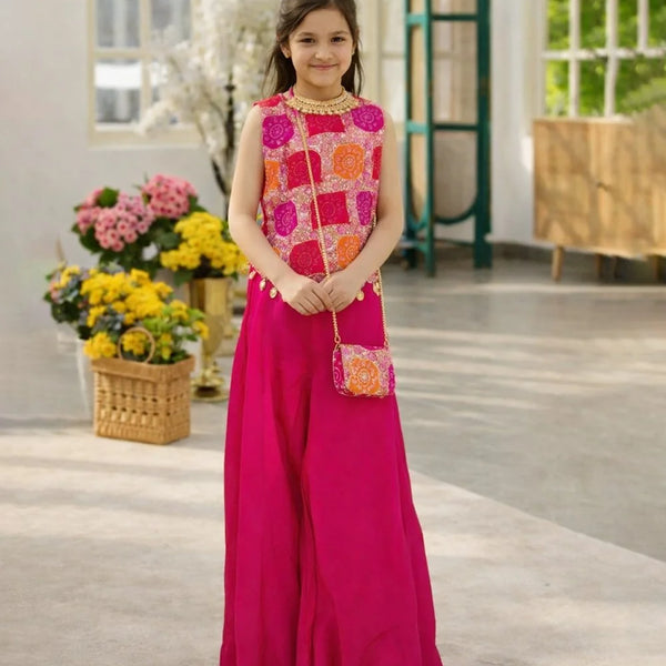 Young girl in a pink and orange traditional outfit standing indoors with flowers in the background.