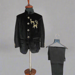 Black velvet suit jacket with gold embroidery on a mannequin and black pants on a hanger against a light wooden background.