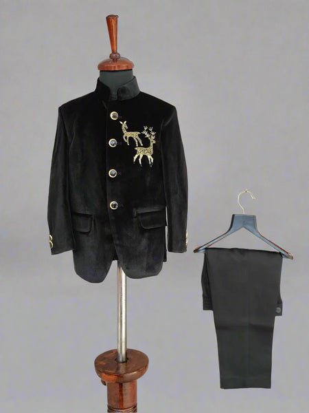 Black velvet suit jacket with gold embroidery on a mannequin and black pants on a hanger against a light wooden background.
