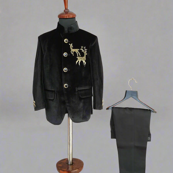 Black velvet suit jacket with gold embroidery on a mannequin and black pants on a hanger against a light wooden background.