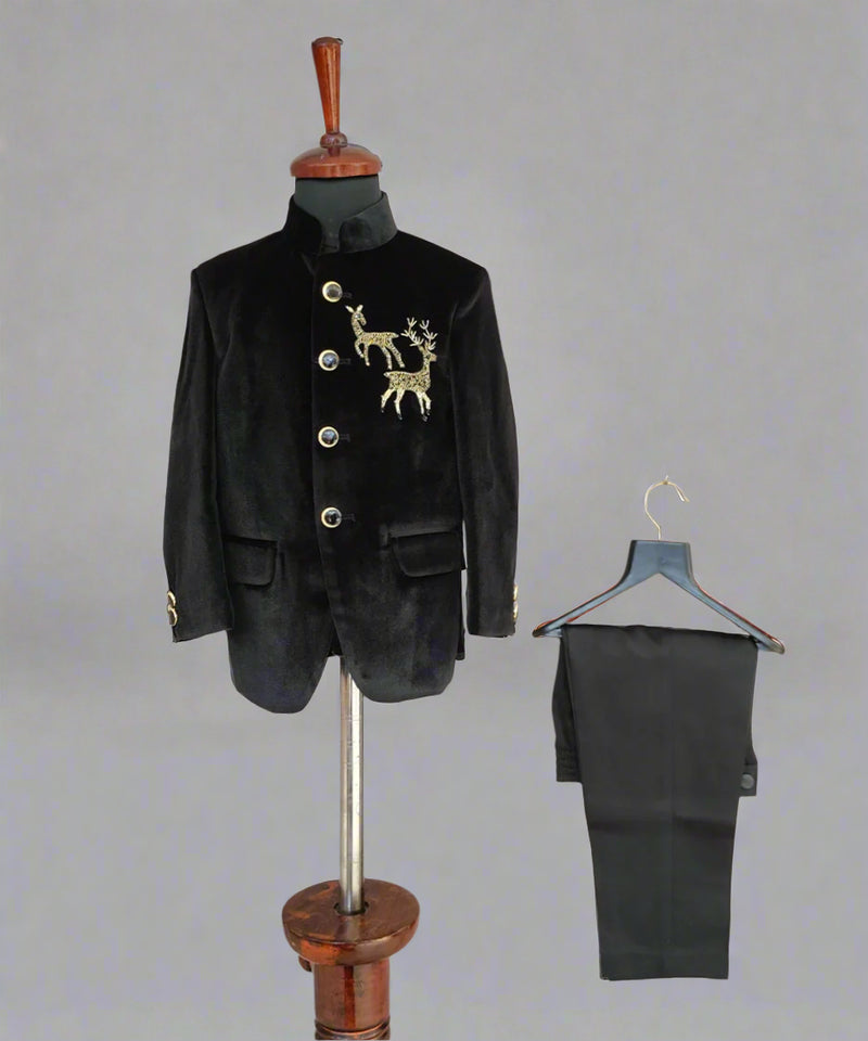 Black velvet suit jacket with gold embroidery on a mannequin and black pants on a hanger against a light wooden background.