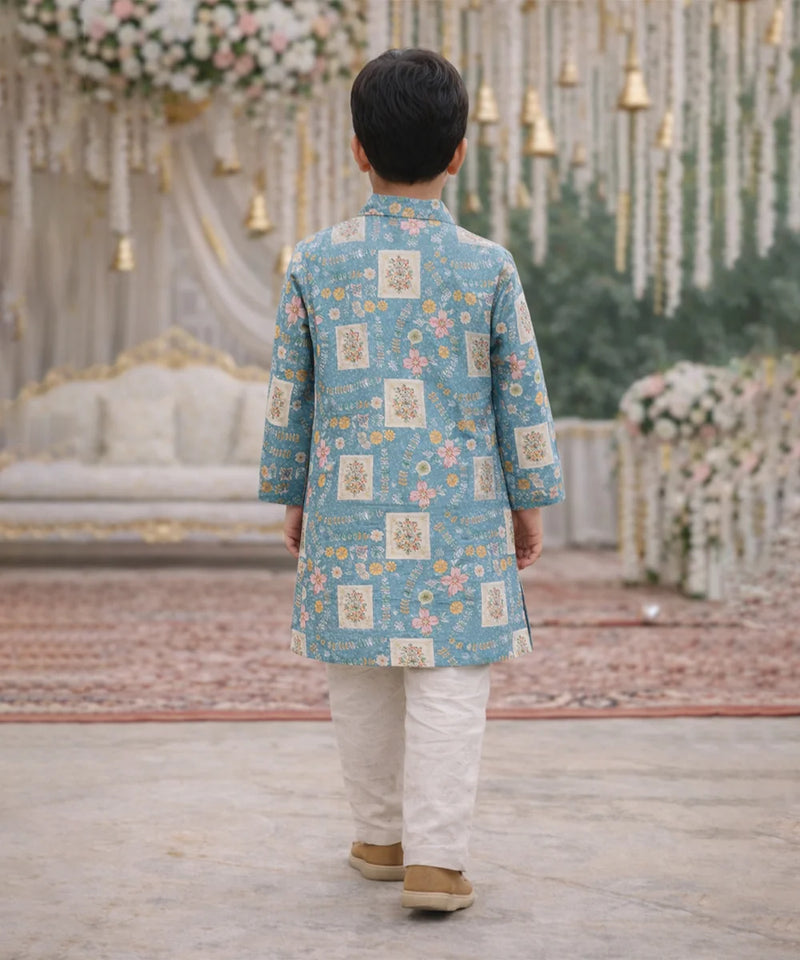 Child wearing a blue floral kurta with white pants in a decorated indoor setting.