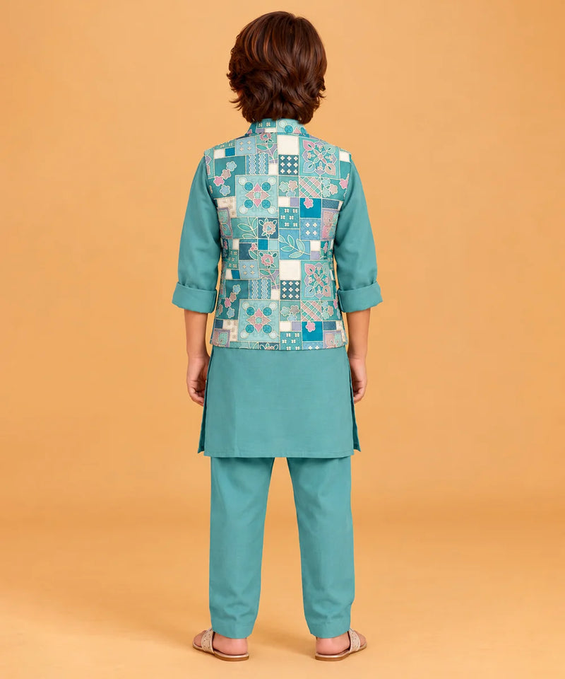 A child model shown from the back wearing a teal-green kurta set with a patterned patchwork vest. The vest features a mix of blue, white, and green geometric and floral motifs.