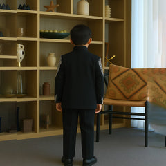 Child in a formal outfit standing in a room with a bookshelf and table.