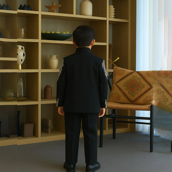 Child in a formal outfit standing in a room with a bookshelf and table.