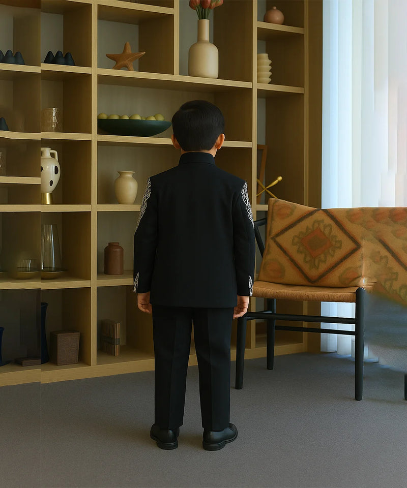 Child in a formal outfit standing in a room with a bookshelf and table.