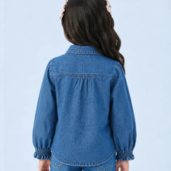 A child model shown from the back wearing a blue denim long-sleeve shirt with gathered cuffs and a button-down collar, paired with matching blue jeans against a light blue studio background.
