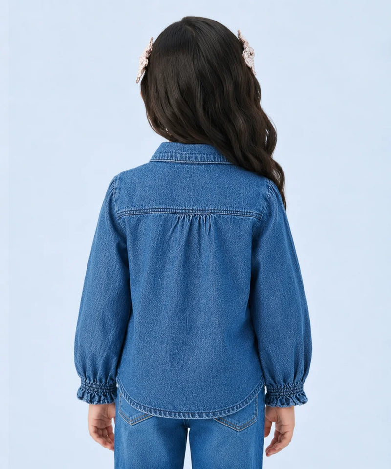 A child model shown from the back wearing a blue denim long-sleeve shirt with gathered cuffs and a button-down collar, paired with matching blue jeans against a light blue studio background.