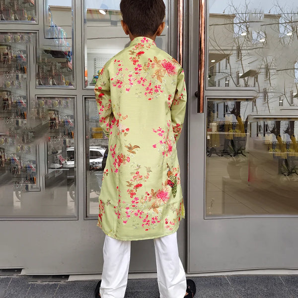 Person wearing a light green floral kurta with white pants standing in front of a glass door.
