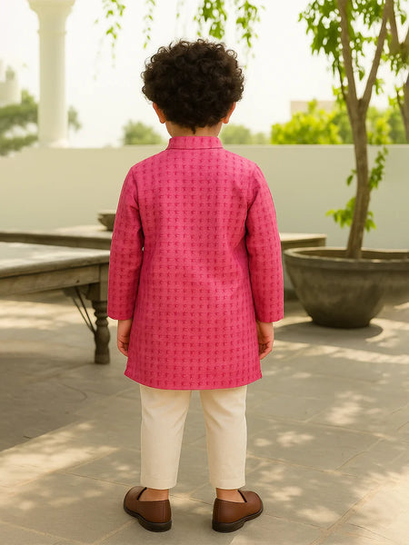 Child wearing a pink traditional outfit standing outdoors with greenery in the background