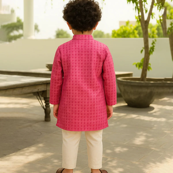Child wearing a pink traditional outfit standing outdoors with greenery in the background
