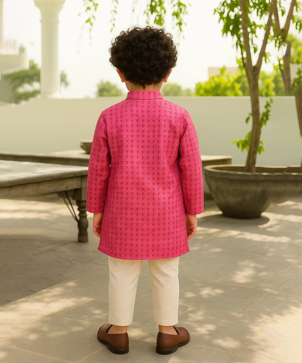Child wearing a pink traditional outfit standing outdoors with greenery in the background