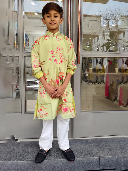 Child wearing a light green kurta with floral patterns standing in front of a glass door.