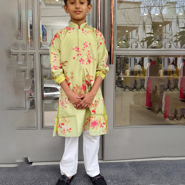 Child wearing a light green kurta with floral patterns standing in front of a glass door.