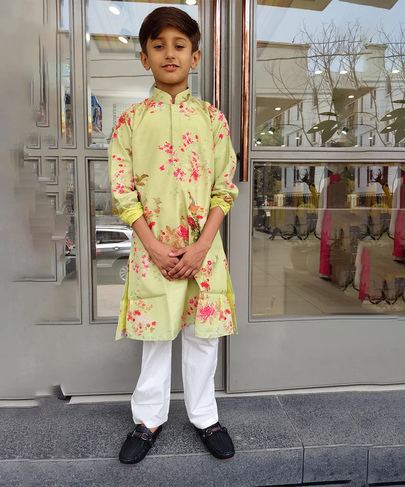 Child wearing a light green kurta with floral patterns standing in front of a glass door.
