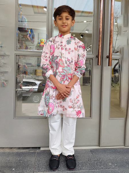 Child wearing a floral kurta with white pants standing in front of a glass door.
