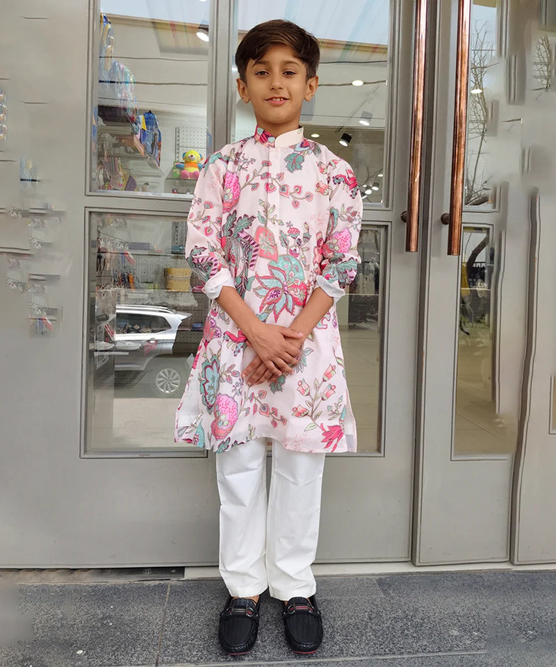 Child wearing a floral kurta with white pants standing in front of a glass door.