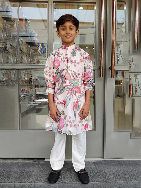 Young boy in a floral kurta standing outside a store.
