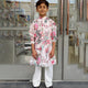 Young boy in a floral kurta standing outside a store.