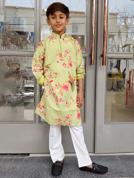 Child wearing a light green floral kurta with white pants standing in front of a glass door.