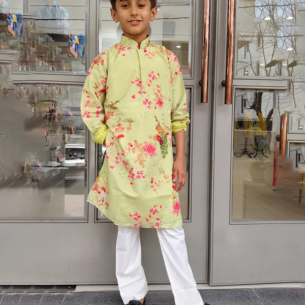 Child wearing a light green floral kurta with white pants standing in front of a glass door.
