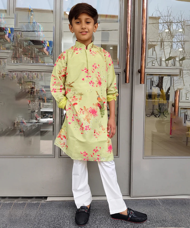 Child wearing a light green floral kurta with white pants standing in front of a glass door.
