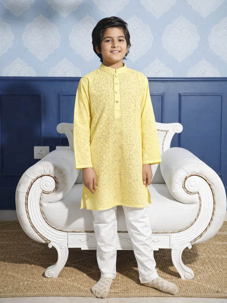 Child wearing a yellow kurta with white pants standing in front of a decorative chair.