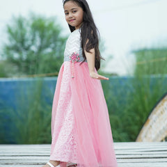 Young girl in a pink and white dress standing outdoors with greenery in the background
