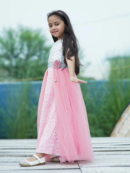 Young girl in a pink and white dress standing outdoors with greenery in the background