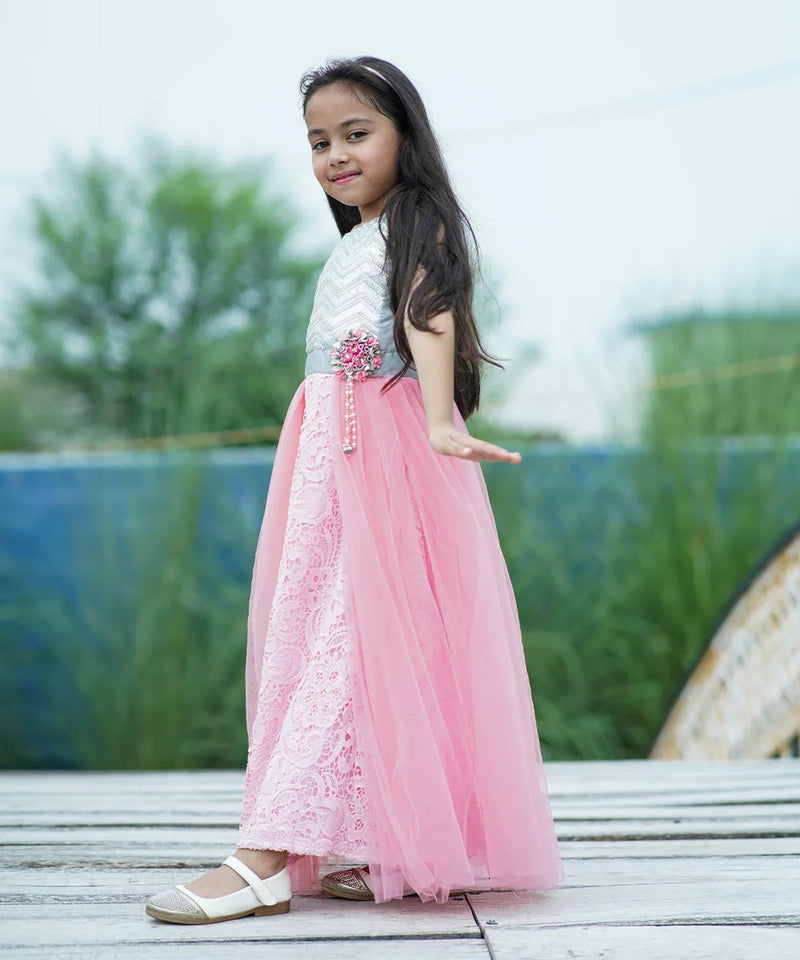 Young girl in a pink and white dress standing outdoors with greenery in the background