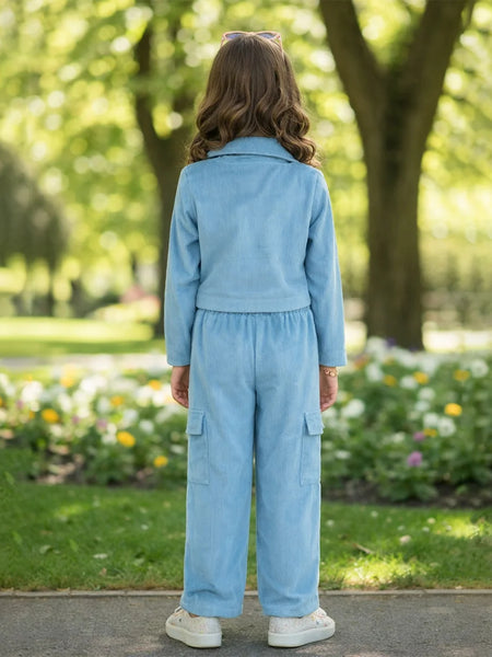 Person wearing a light blue outfit standing in a park with greenery and flowers.