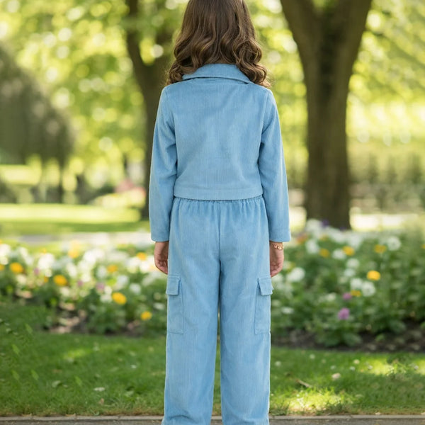 Person wearing a light blue outfit standing in a park with greenery and flowers.