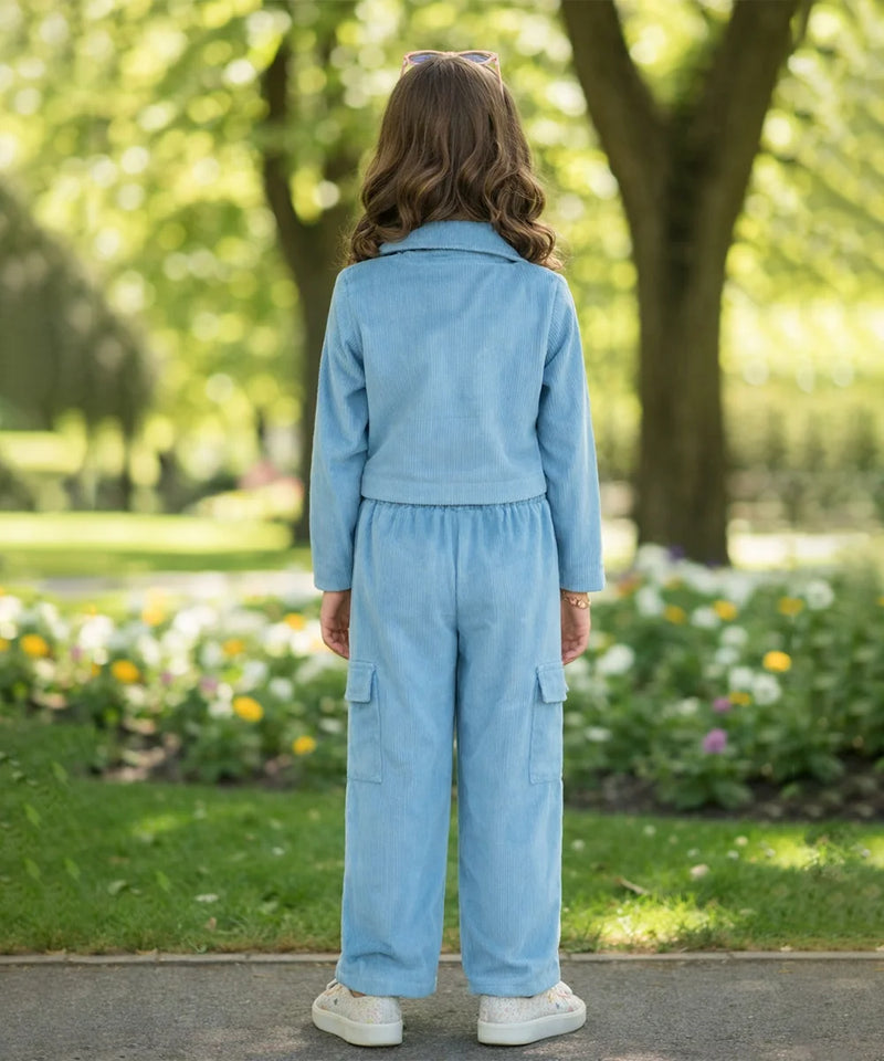Person wearing a light blue outfit standing in a park with greenery and flowers.