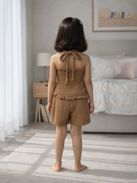 Young girl in a brown knitted outfit standing in a bedroom.