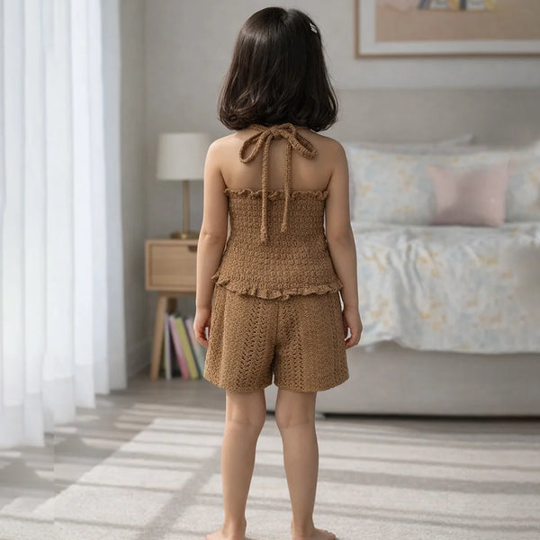 Young girl in a brown knitted outfit standing in a bedroom.