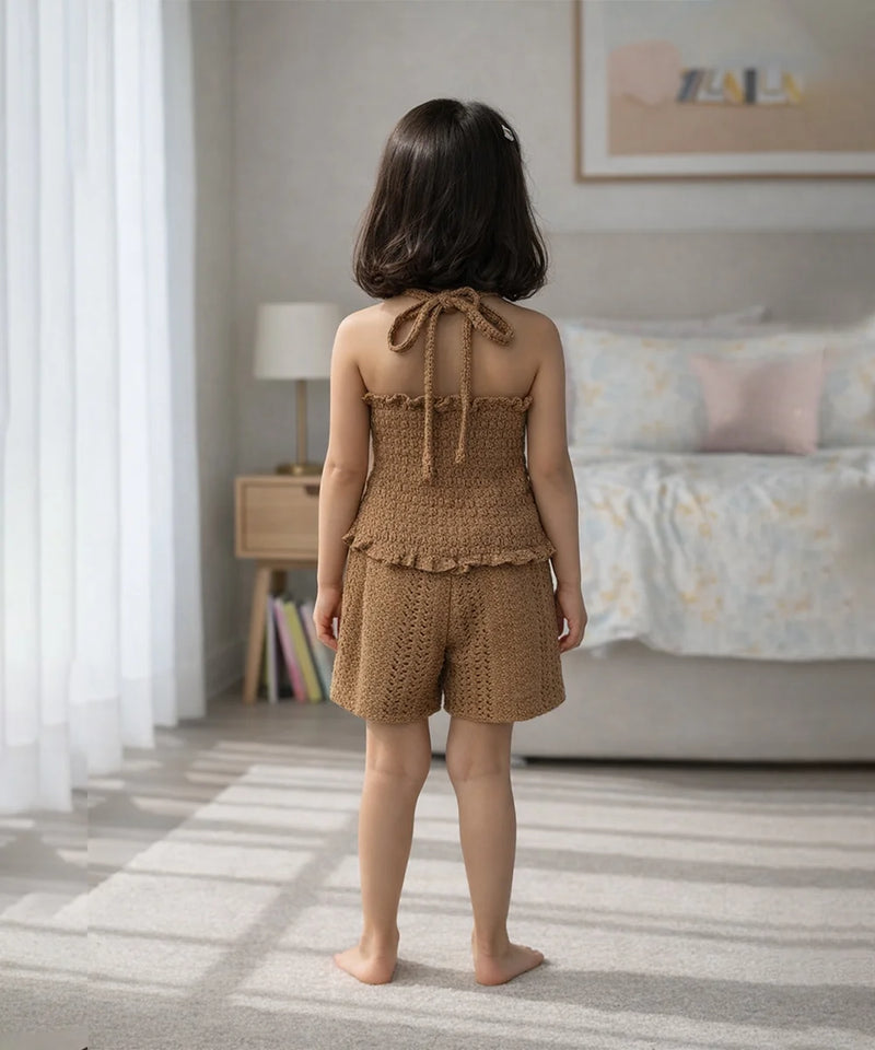 Young girl in a brown knitted outfit standing in a bedroom.