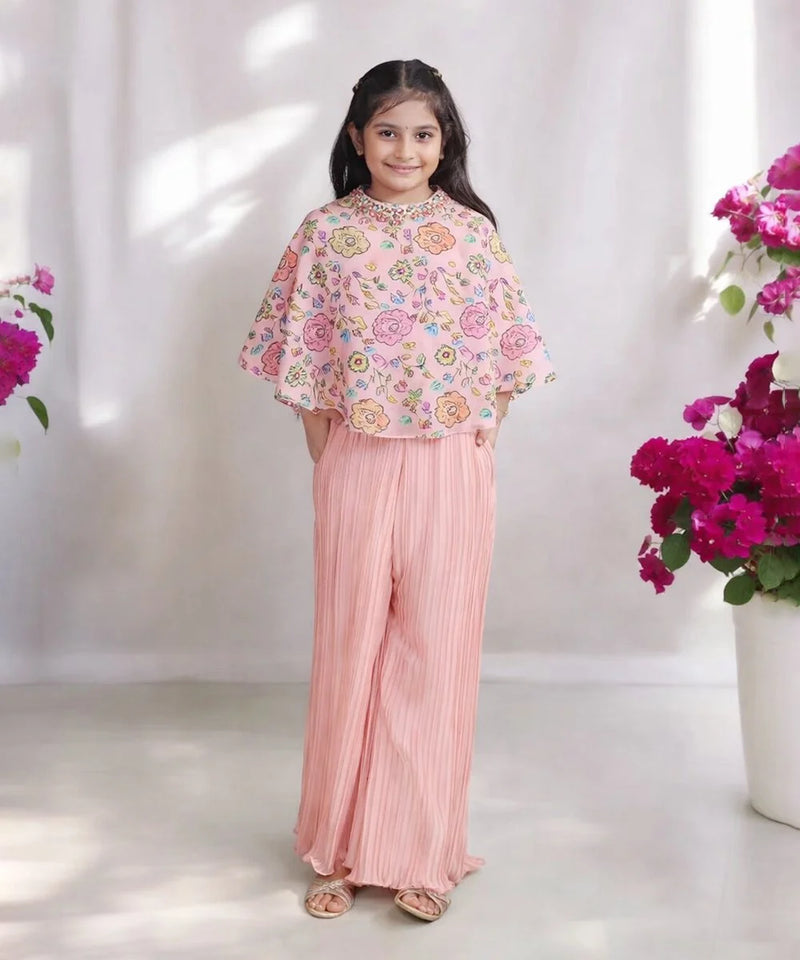 Young girl in a floral top and pink pants standing between two flower arrangements on a white background