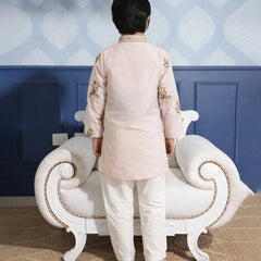 Person wearing a traditional outfit standing in front of a decorative wall and white sofa.