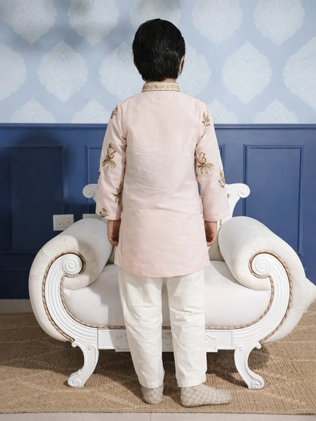 Person wearing a traditional outfit standing in front of a decorative wall and white sofa.