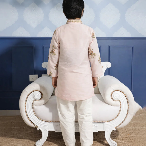 Person wearing a traditional outfit standing in front of a decorative wall and white sofa.