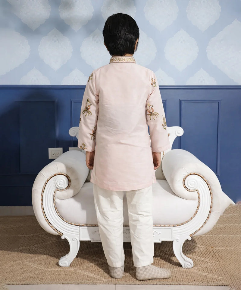 Person wearing a traditional outfit standing in front of a decorative wall and white sofa.